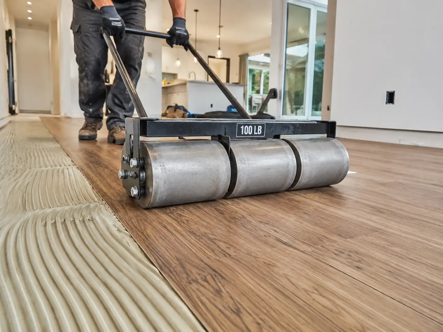 Professional installer using a heavy 100-pound floor roller to press glue down vinyl planks into adhesive